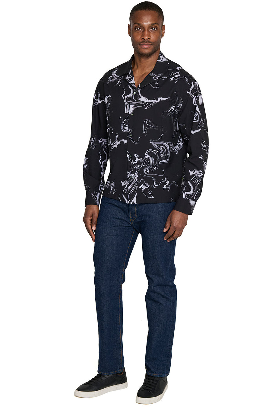 Man wearing a black patterned shirt and blue jeans on a white background